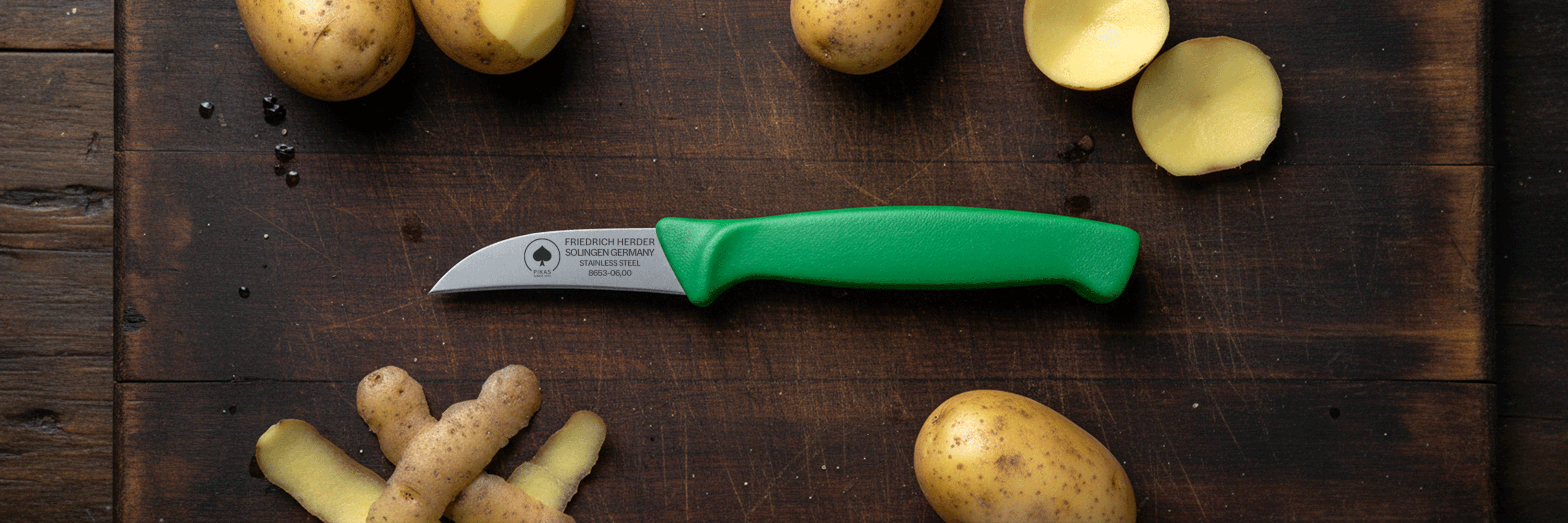 Schälmesser mit grünem Kunststoffgriff von Friedrich Herder aus Solingen, liegt auf einem dunklen Holzbrett mit geschälten und ungeschälten Kartoffeln – hochwertiges Solinger Schälmesser aus Edelstahl für präzises Schälen von Kartoffeln und Gemüse.