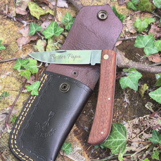 Hippekniep Taschenmesser mit Holzgriff und individueller Gravur liegt auf moosigem Holz in natürlicher Outdoor-Umgebung.