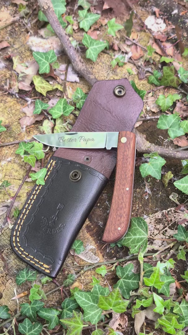 Hippekniep Taschenmesser mit Holzgriff und individueller Gravur liegt auf moosigem Holz in natürlicher Outdoor-Umgebung.
